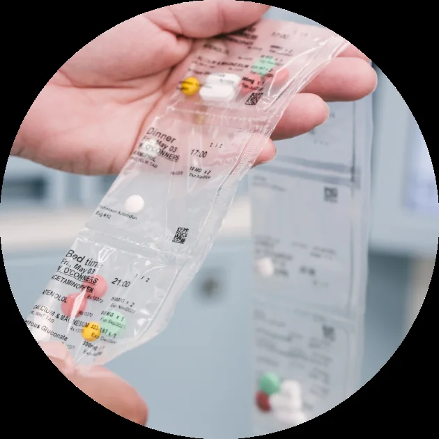A hand holding a connected strip of filled Pac-Med medication pouches, each labelled by day and dose time